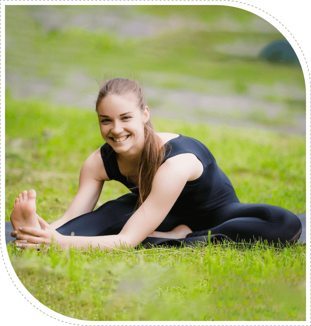 Woman stretching outdoors on grass, smiling happily.